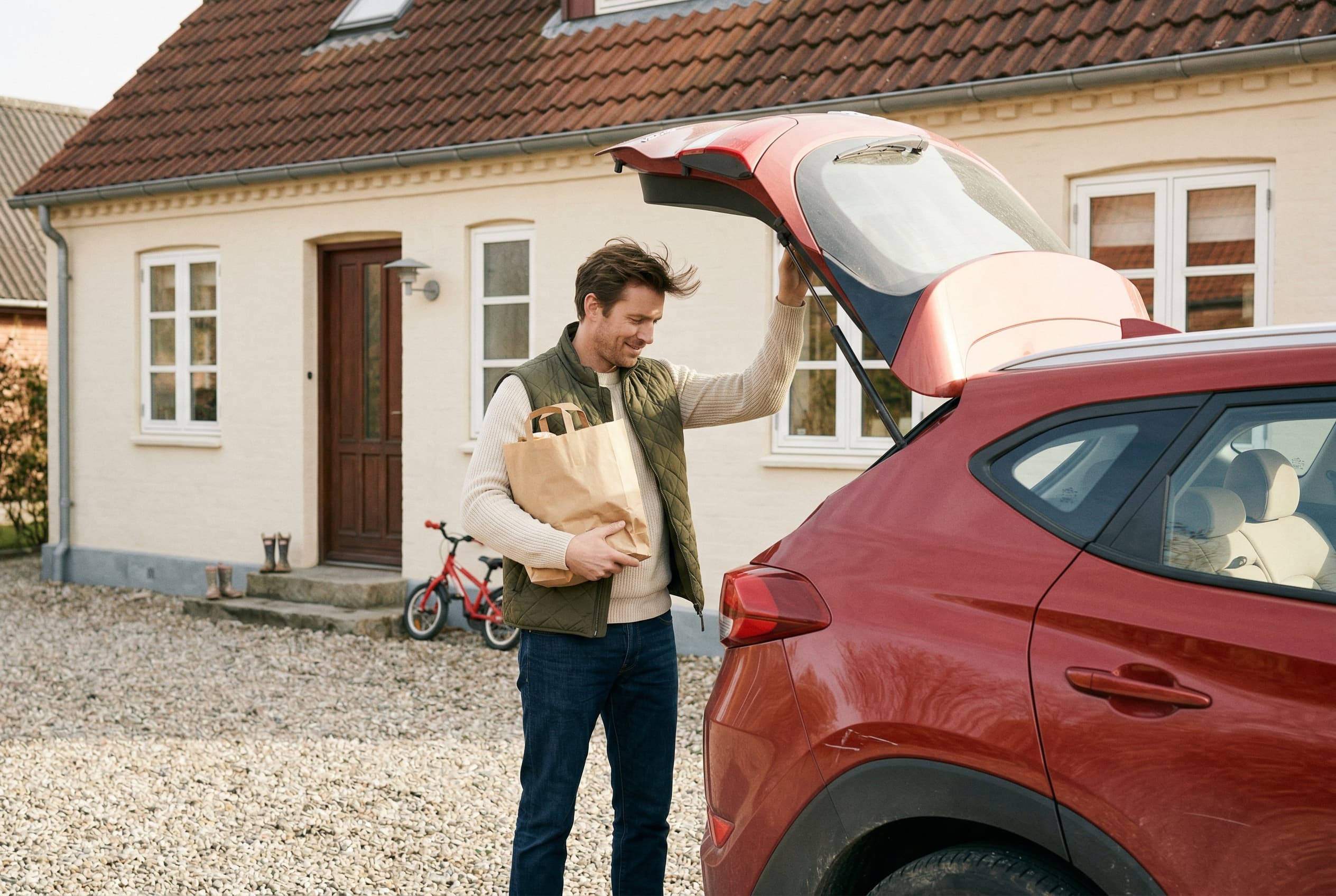 Mand lukker bagklap på rød bil med indkøb